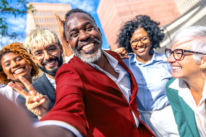 Những người thuộc nhiều độ tuổi, chủng tộc và giới tính khác nhau đang tươi cười rạng rỡ trước một tòa nhà.